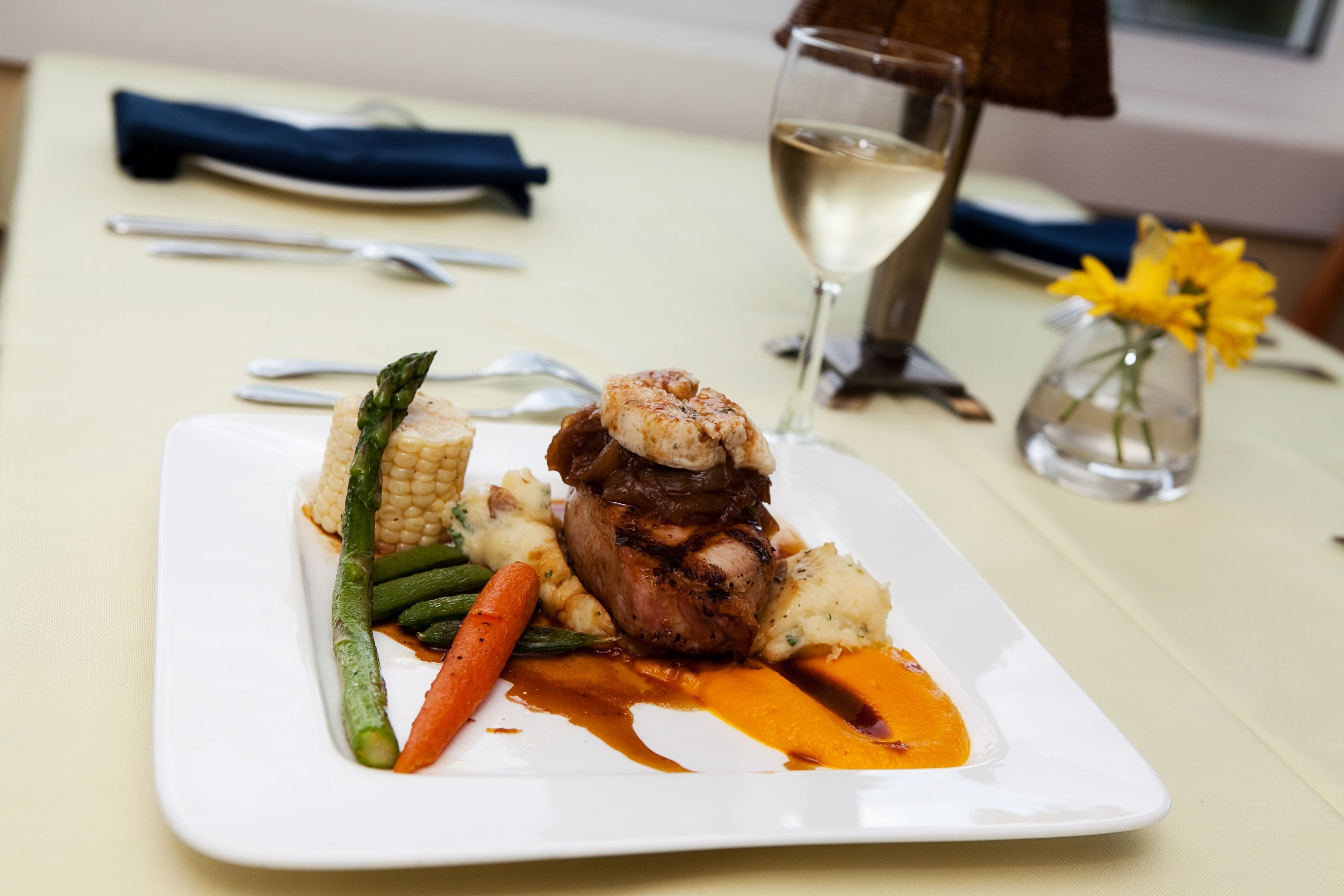 A plate of food with vegetables and a glass of white wine on a table.
