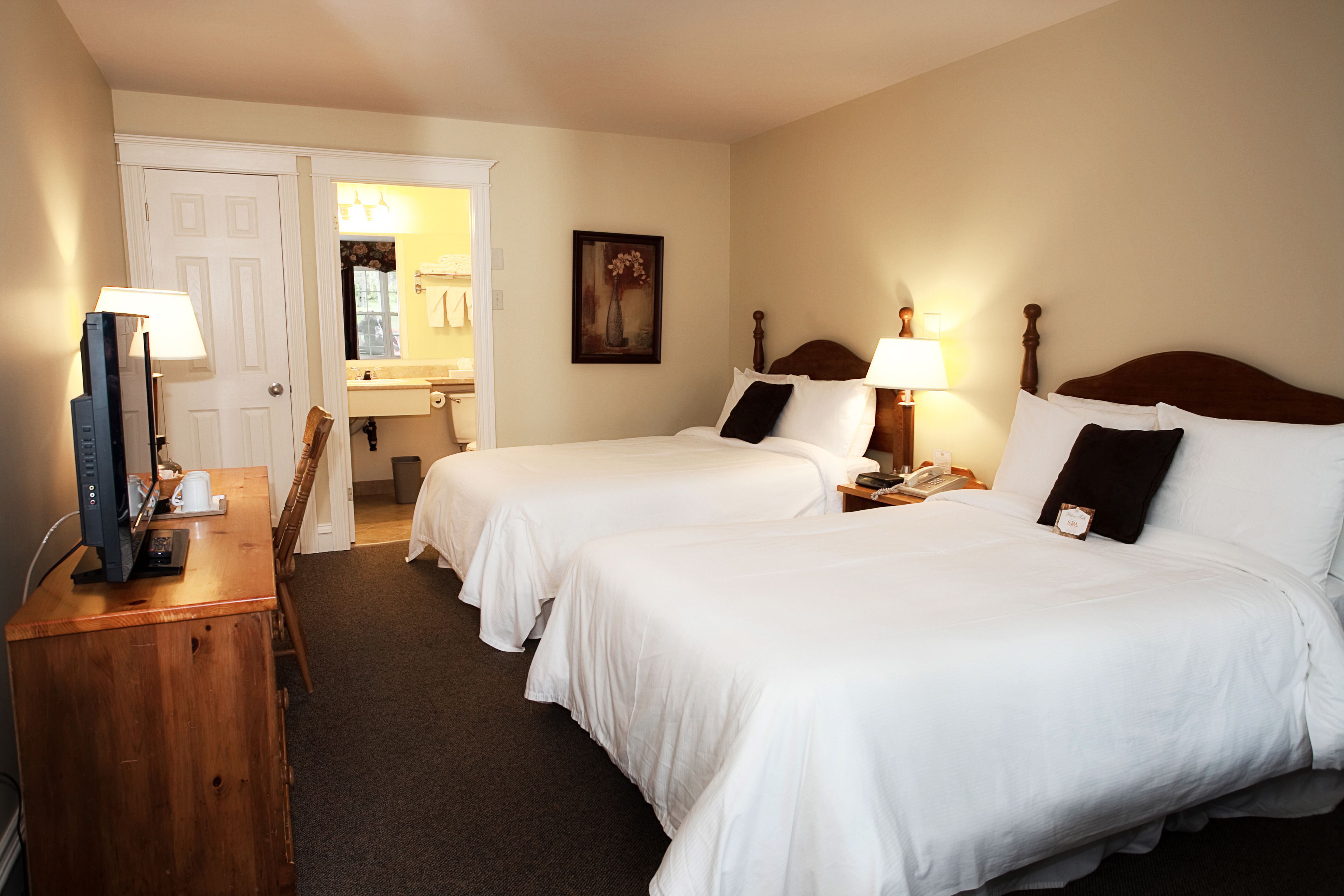 Une chambre d’hôtel avec deux lits, un bureau avec un ordinateur, une chaise et une salle de bain visible à travers une porte ouverte.