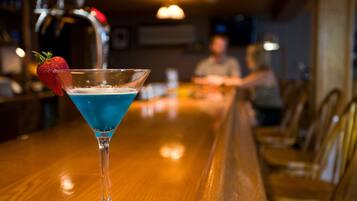 Un verre à martini contenant un liquide bleu et décoré d’une fraise, posé sur le comptoir en bois d’un bar.