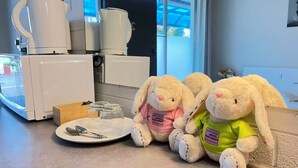 Una kitchenette con una cafetera, un plato con utensilios y dos conejos de peluche.