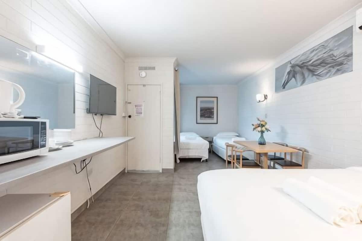 A hotel room with a bed, a desk with a computer, a small table with a vase, and a TV mounted on the wall.