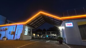Entrada de un hotel con un letrero de neón, un área de estacionamiento y un edificio con el número 768.