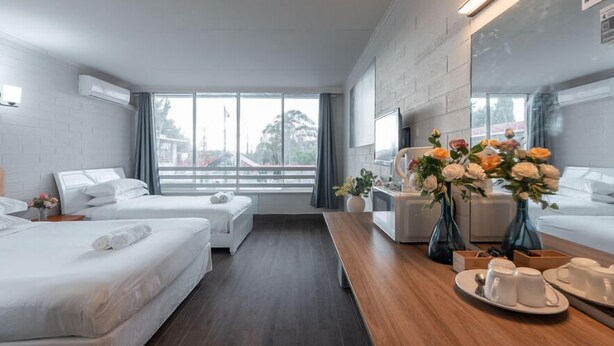 Habitación de hotel moderna con dos camas, una mesa de comedor de madera y un ventanal con vistas al exterior.