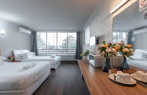 A modern hotel room with two beds, a wooden dining table, and a large window offering a view of the outside. - Motel Maroondah (Mont Albert)