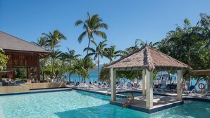 A clear pool with lounge chairs and a gazebo, surrounded by palm trees and a view of the ocean. - Fitzroy Island Resort (Fitzroy Island)