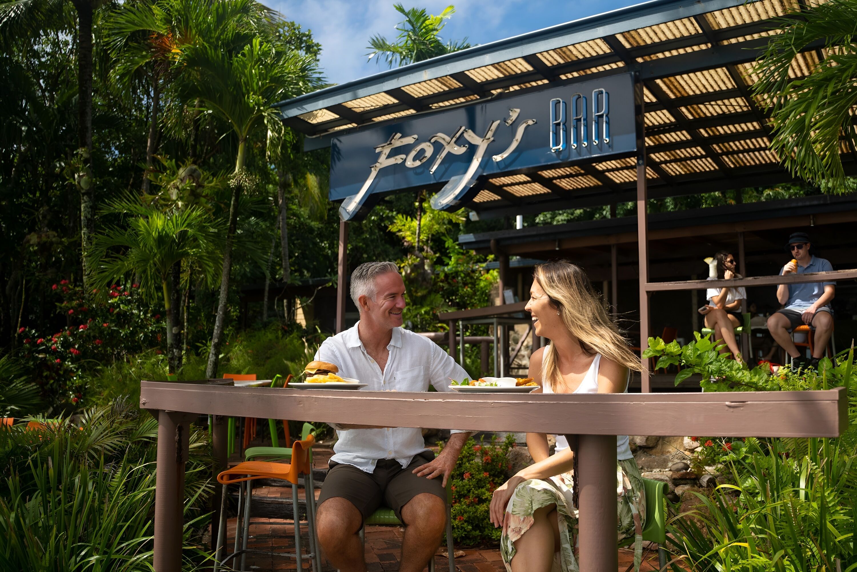 Un restaurante llamado "Foxy's Bar" con terraza al aire libre rodeado de exuberante follaje.