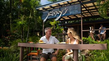 Un restaurante llamado "Foxy's Bar" con terraza al aire libre rodeado de exuberante follaje.