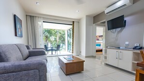 A modern living room with a grey sofa, a wooden coffee table, a flat-screen TV mounted on the wall, and a kitchen area with white cabinets. - Fitzroy Island Resort (Fitzroy Island)