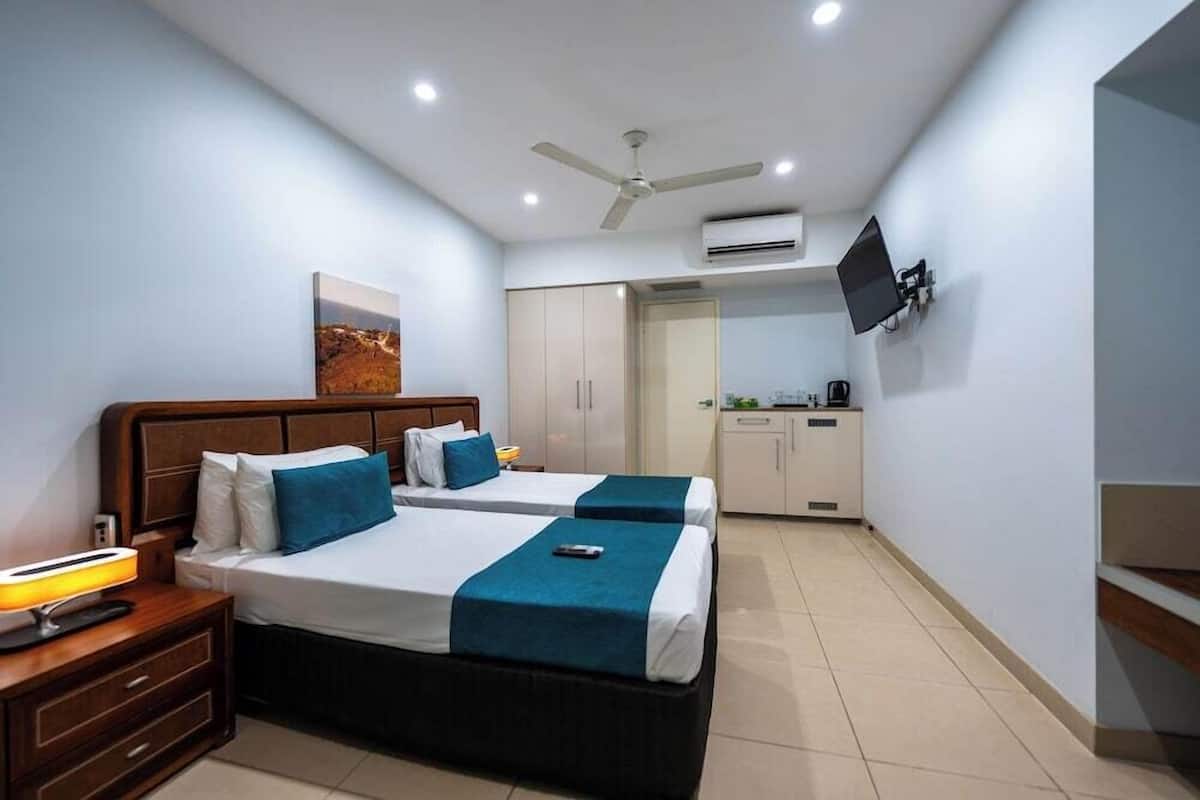 A hotel room with two beds, a desk, a chair, a TV mounted on the wall, and a ceiling fan.