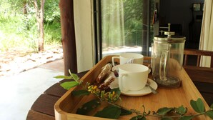 A wooden tray with two white cups and a glass coffee pot on a table near a window overlooking a forest. - Shikwari Nature Reserve (Hoedspruit)
