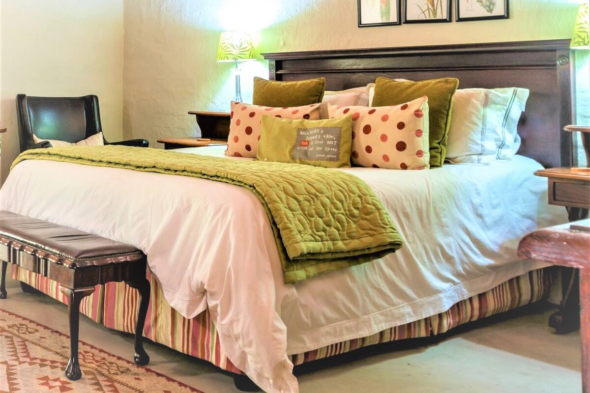Un dormitorio ordenado con una cama, almohadas, un banco y una mesita de noche.