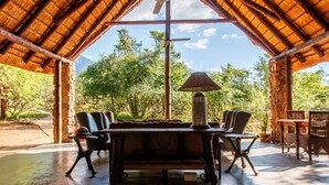 An outdoor patio with a thatched roof, a dining table with chairs, and a decorative lamp. - Shikwari Nature Reserve (Hoedspruit)