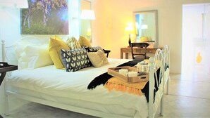 A bedroom with a bed, pillows, a bedside table, a lamp, a mirror, and a window with a view of trees. - Shikwari Nature Reserve (Hoedspruit)