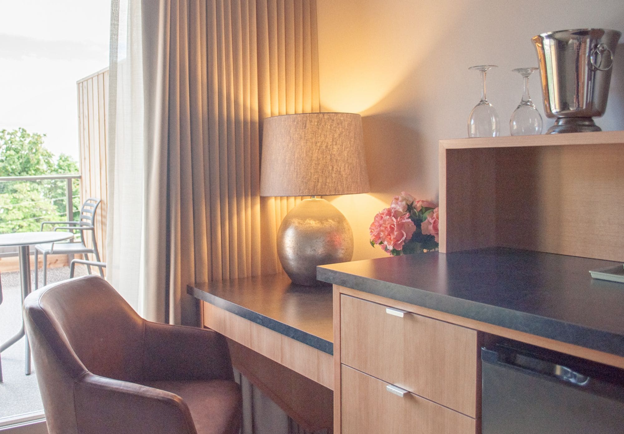 A modern kitchen with a wooden countertop, a lamp, a vase with flowers, and a wine glass set.