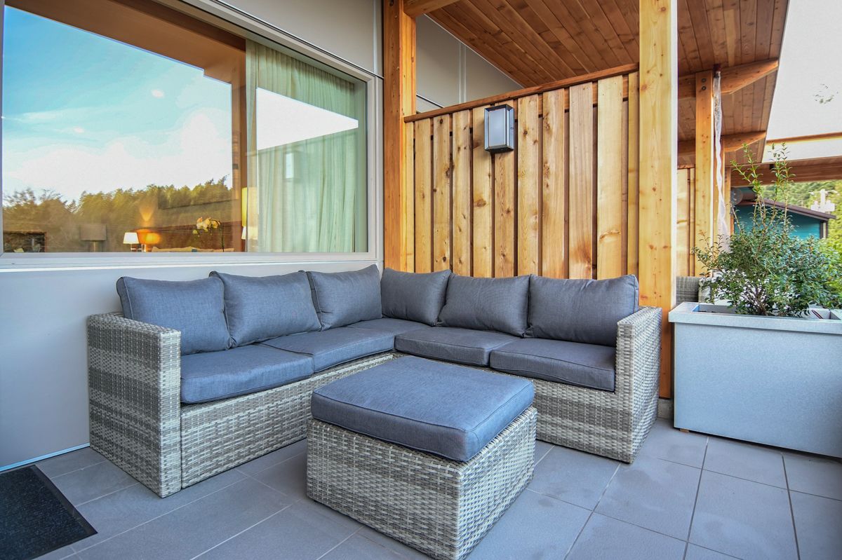 A modern outdoor seating area with a wicker sectional sofa and ottoman, a wooden pergola, and a view of the surrounding landscape.
