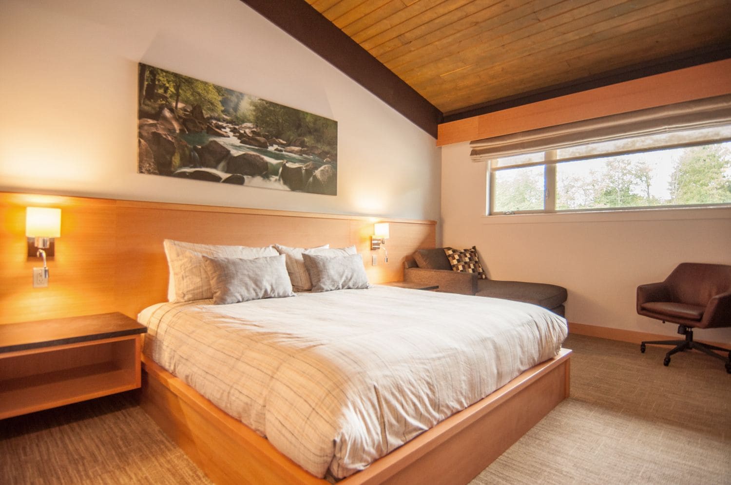 A bedroom with a large bed, bedside lamps, a window, and a painting of a river.