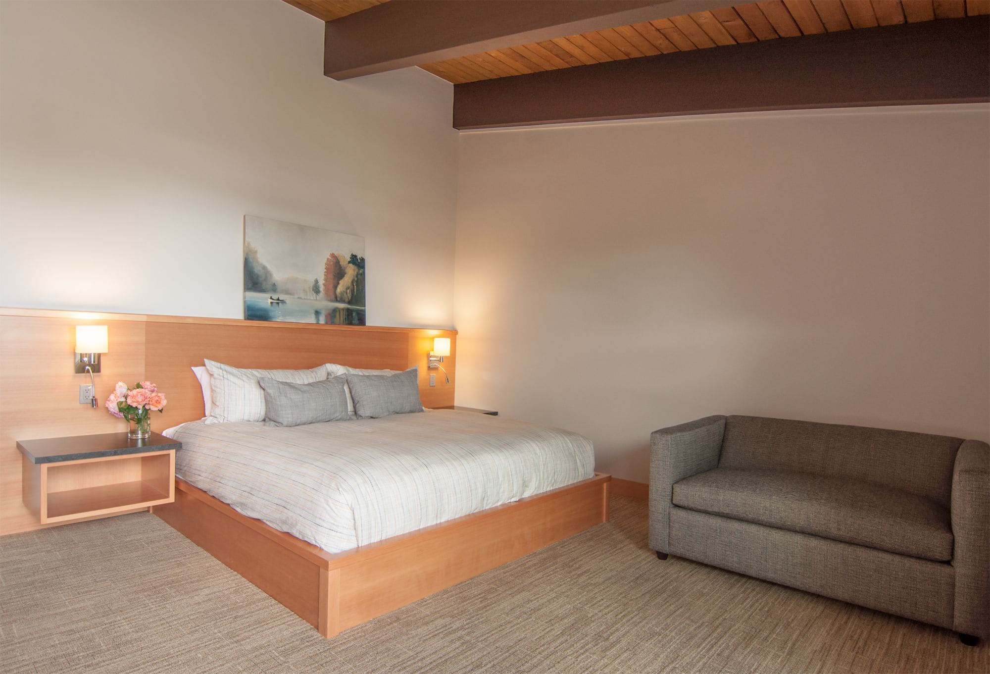 A bedroom with a bed, bedside tables, a nightstand, a sofa, and a painting on the wall.