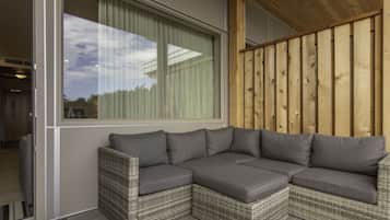 A corner sectional sofa with grey cushions, a wicker frame, and a view through a large window with curtains.