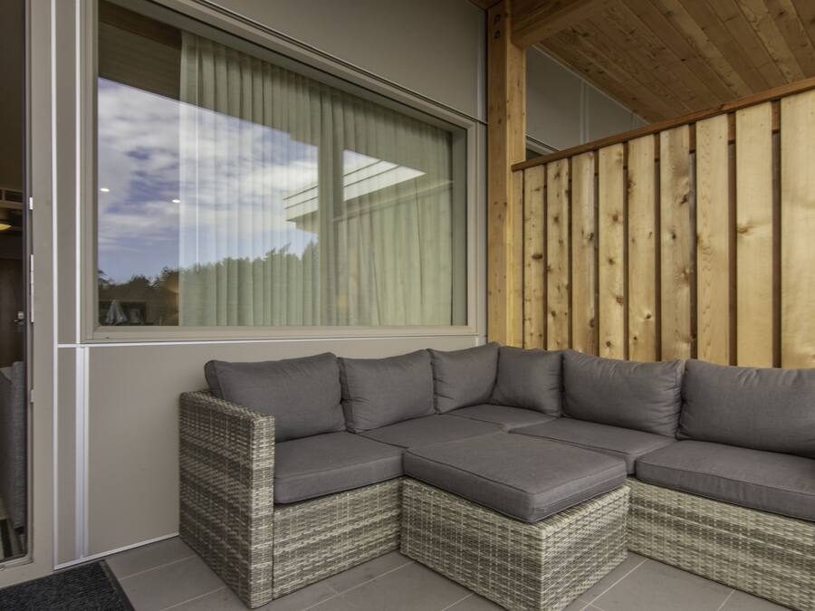 A corner sectional sofa with grey cushions, a wicker frame, and a view through a large window with curtains.