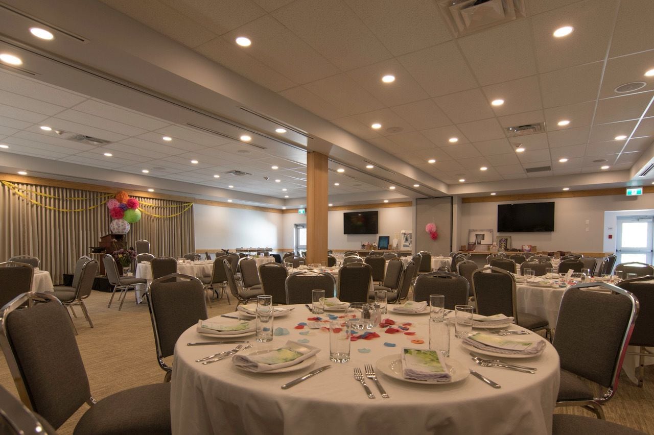 A banquet hall with round tables set for dining, equipped with plates, cutlery, and glasses.