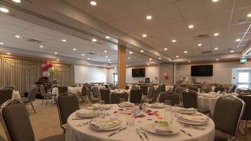 A banquet hall with round tables set for dining, equipped with plates, cutlery, and glasses.