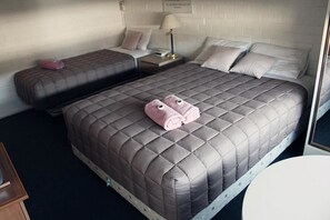A hotel room with a large bed, two smaller beds, a bedside table with a lamp, and a round table. - H&D Apartments (St Kilda)