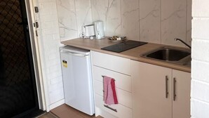 A compact kitchen with white cabinets, a microwave, a coffee maker, and a sink. - H&D Apartments (St Kilda)