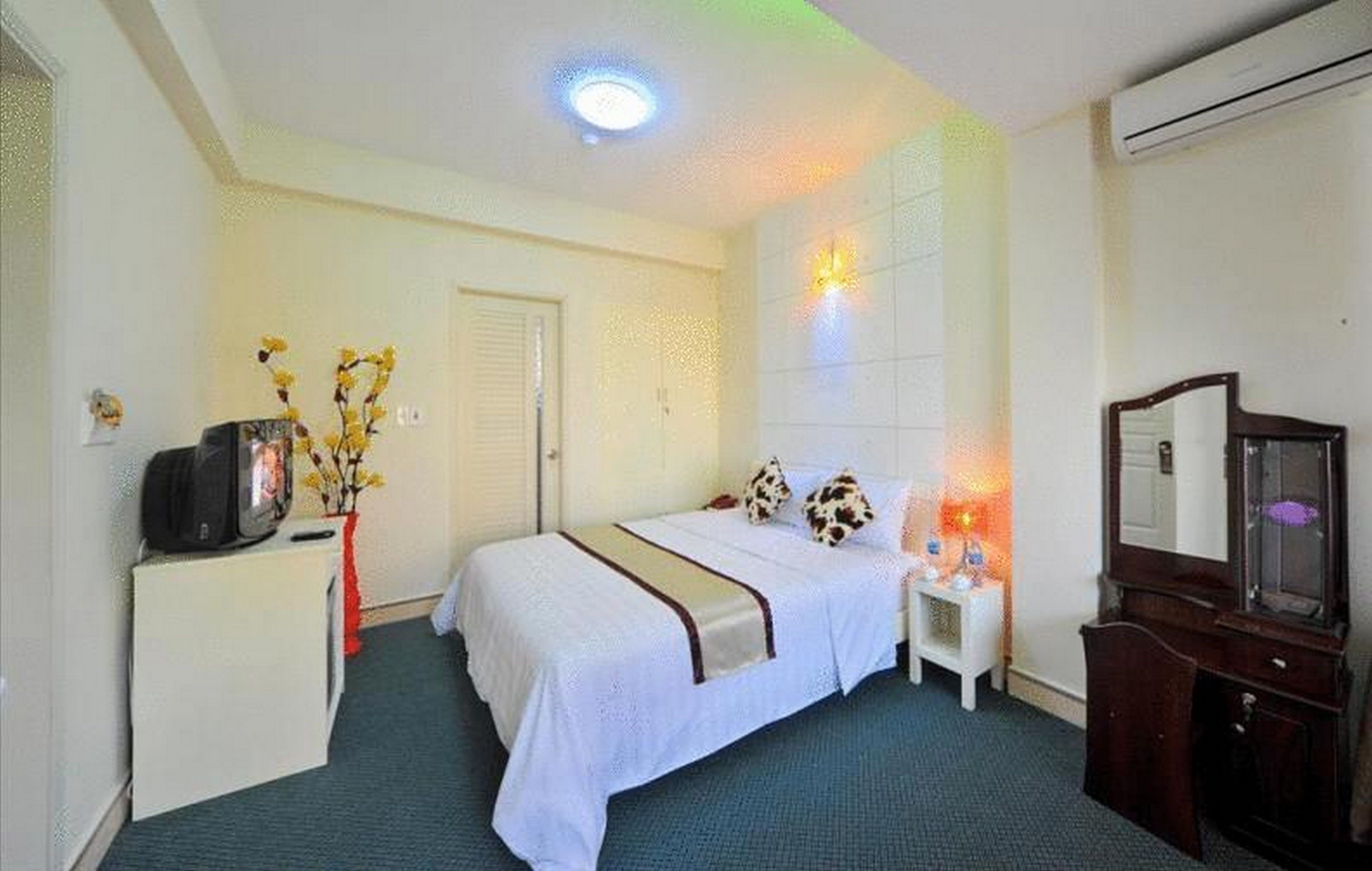 A hotel room with a bed, bedside table, TV, and a mirror.
