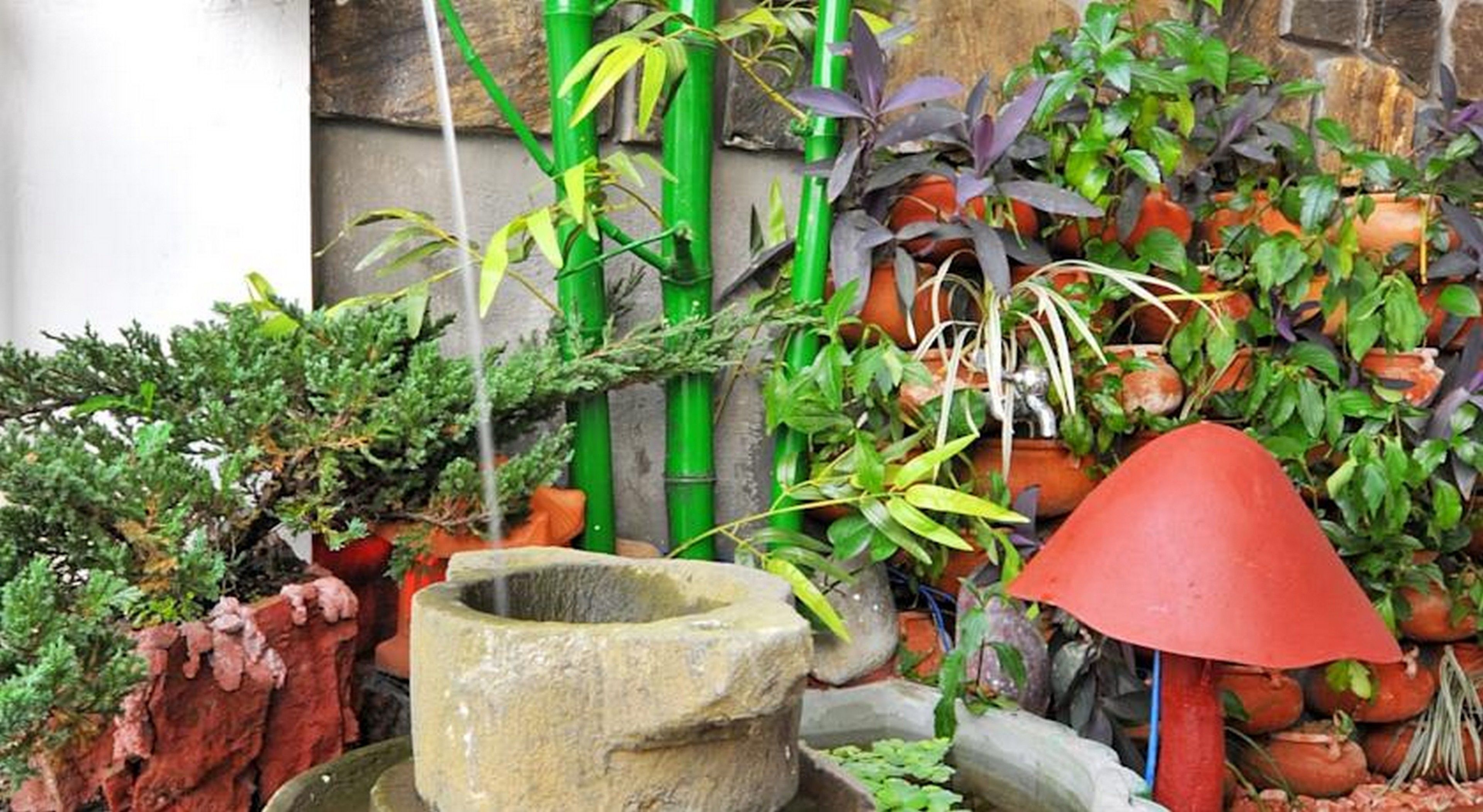 A garden with a stone fountain, various potted plants, and a red umbrella.