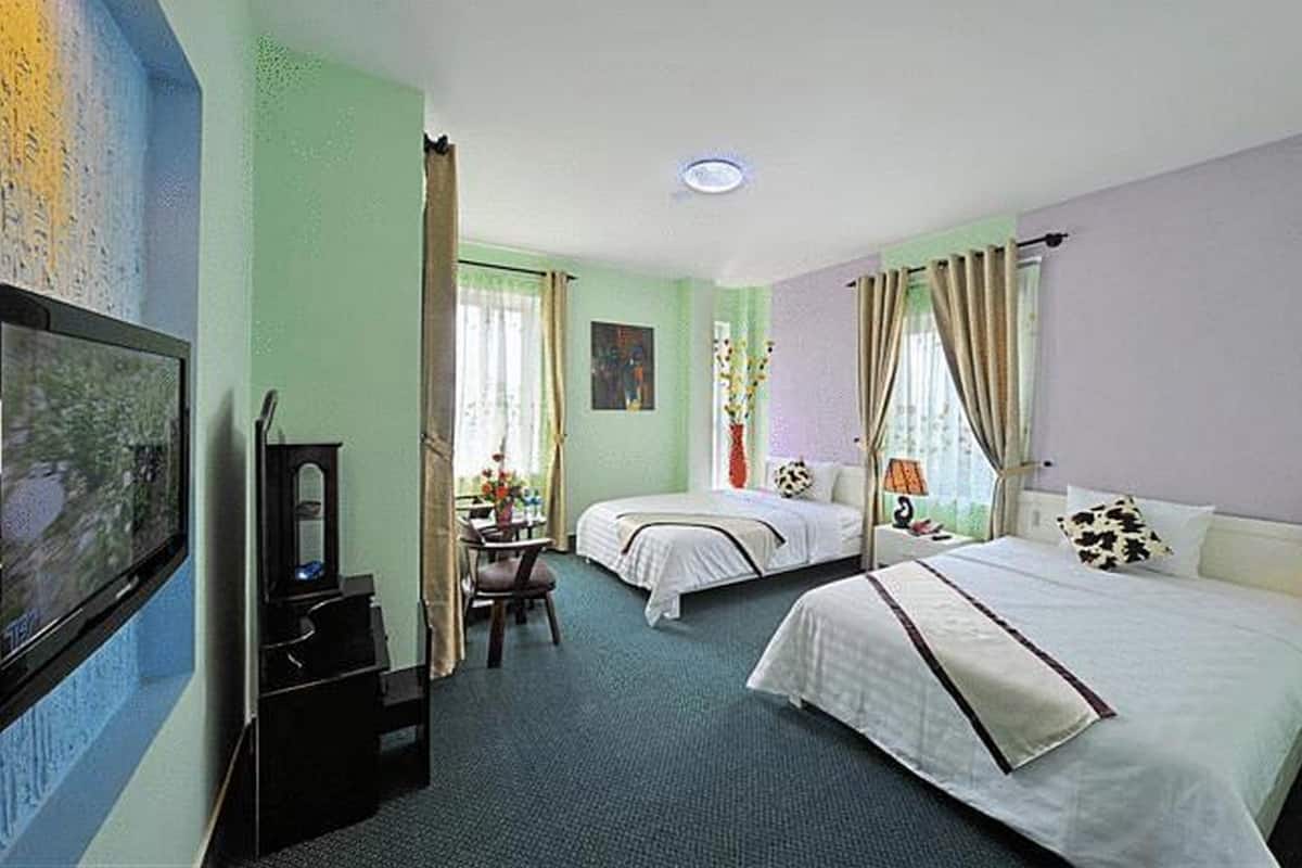 Habitación de hotel con dos camas, un escritorio, una silla, un televisor y una ventana con cortinas.