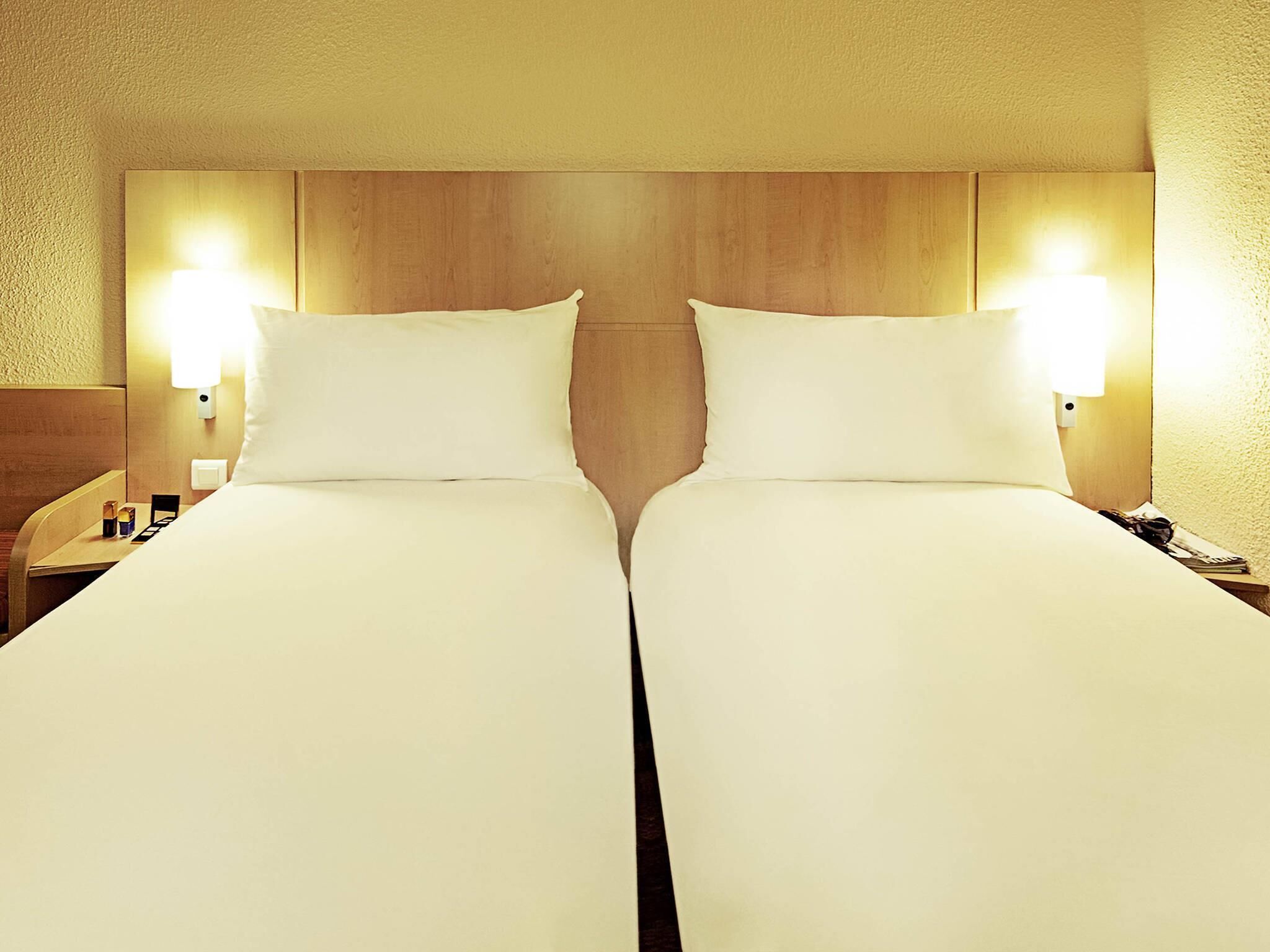 A hotel room with two beds, wooden headboard, bedside lamps, and a nightstand.