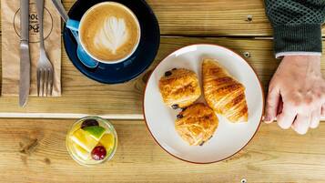 A wooden table with a plate of croissants, a cup of coffee with latte art, and a glass of fruit juice.