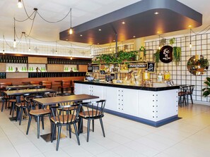 A modern cafe interior with a central counter, seating area, and a wall displaying various items. - ibis Oviedo (Oviedo)