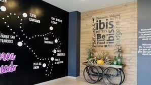 Un vestíbulo de hotel con una pared negra que presenta un mapa de San Francisco, una pared de madera con un letrero de bienvenida y una silla de ruedas con un arreglo floral.