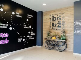 Un vestíbulo de hotel con una pared negra que presenta un mapa de San Francisco, una pared de madera con un letrero de bienvenida y una silla de ruedas con un arreglo floral.