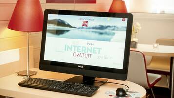 Un monitor de computadora mostrando un sitio web de hotel con el texto 'Internet gratis', un teclado, un ratón y una lámpara roja sobre un escritorio.