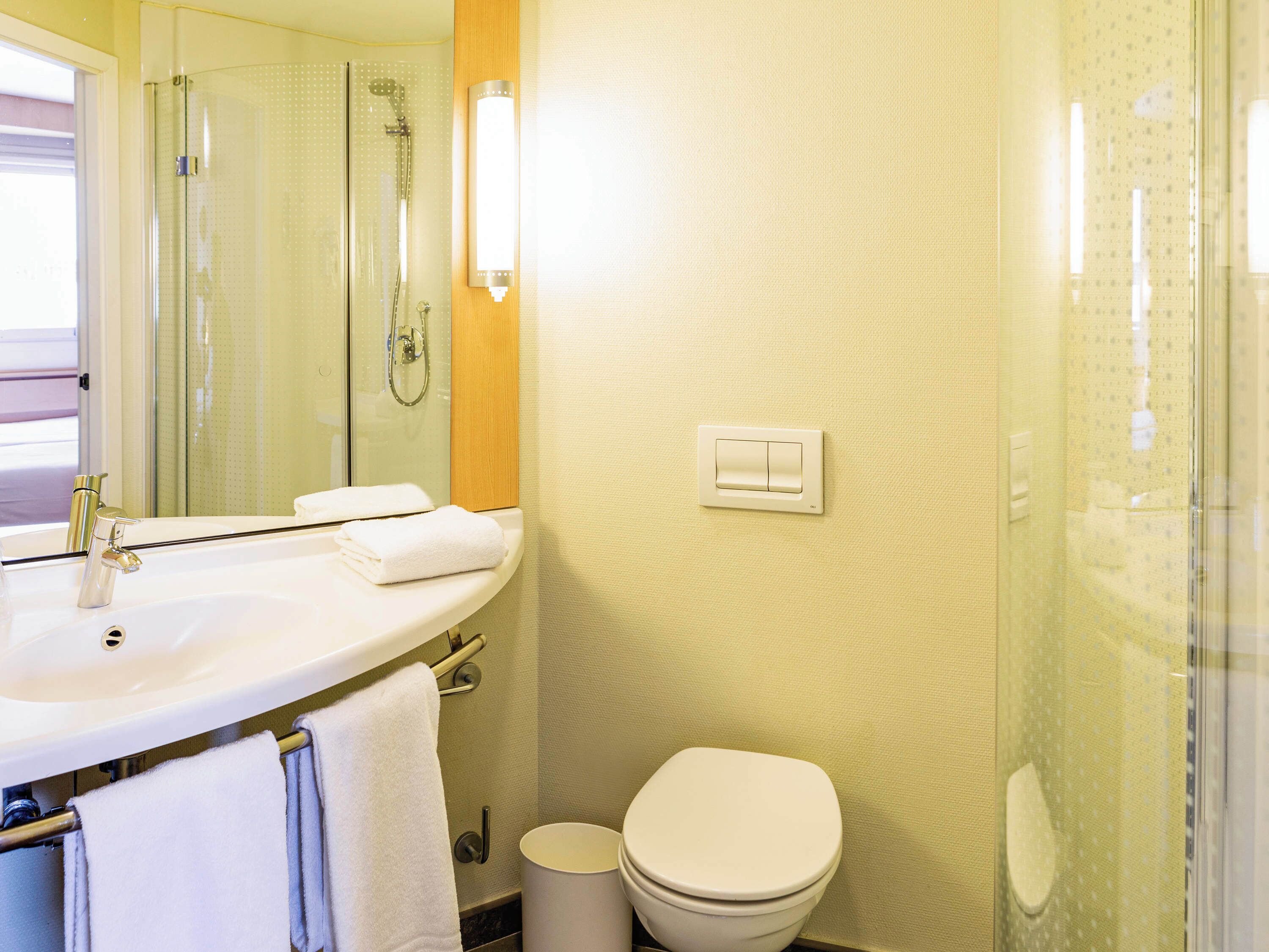 Une salle de bain équipée d’un lavabo, d’un miroir, d’un porte-serviettes, d’une douche et de toilettes.
