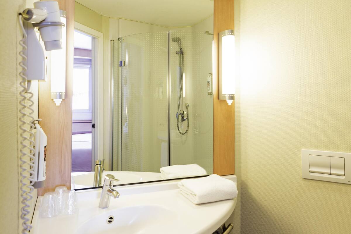 Un baño con lavamanos, espejo, toallero y ducha.