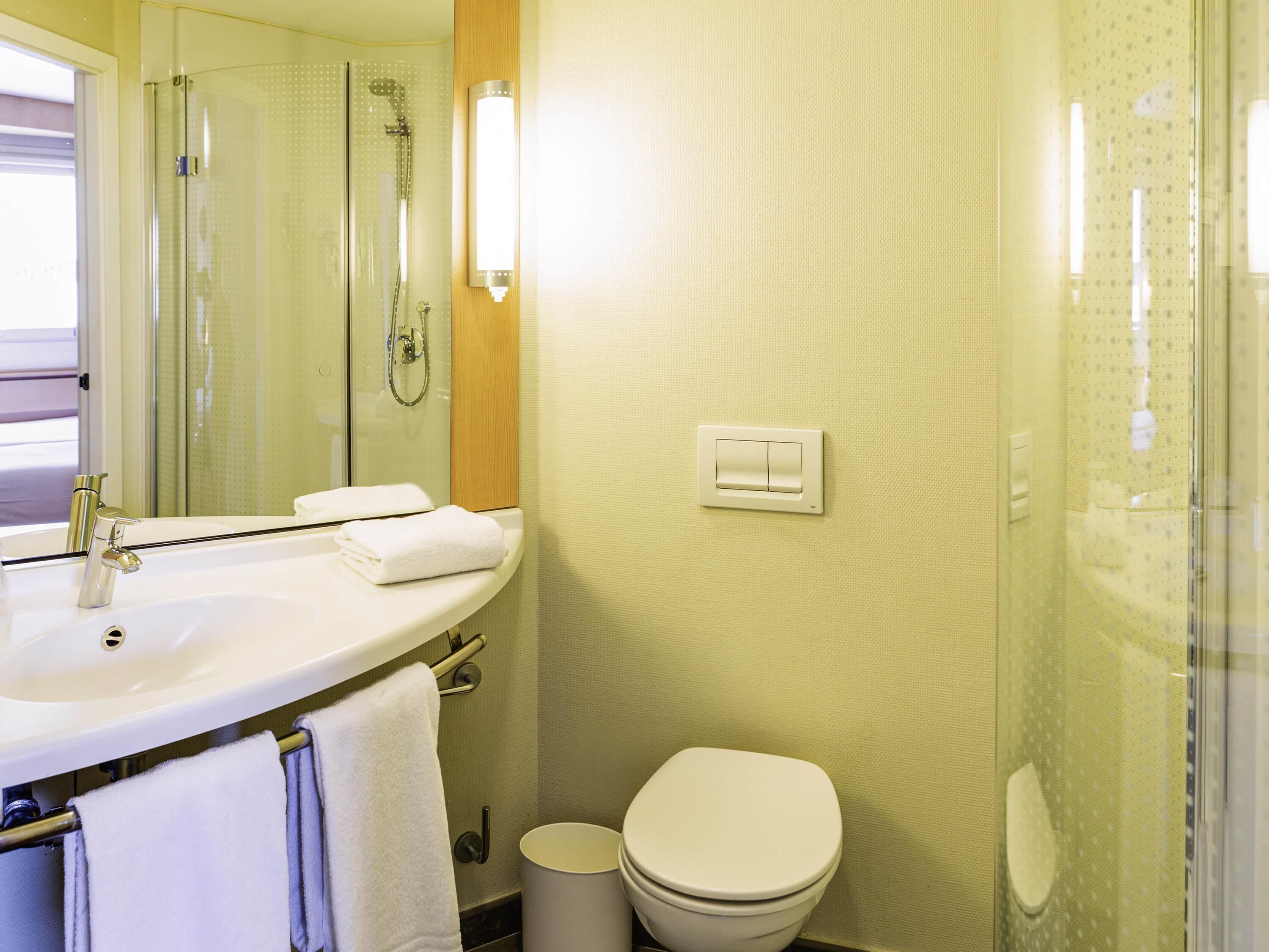 A bathroom with a white sink, a mirror, a towel rack, a toilet, and a shower area.