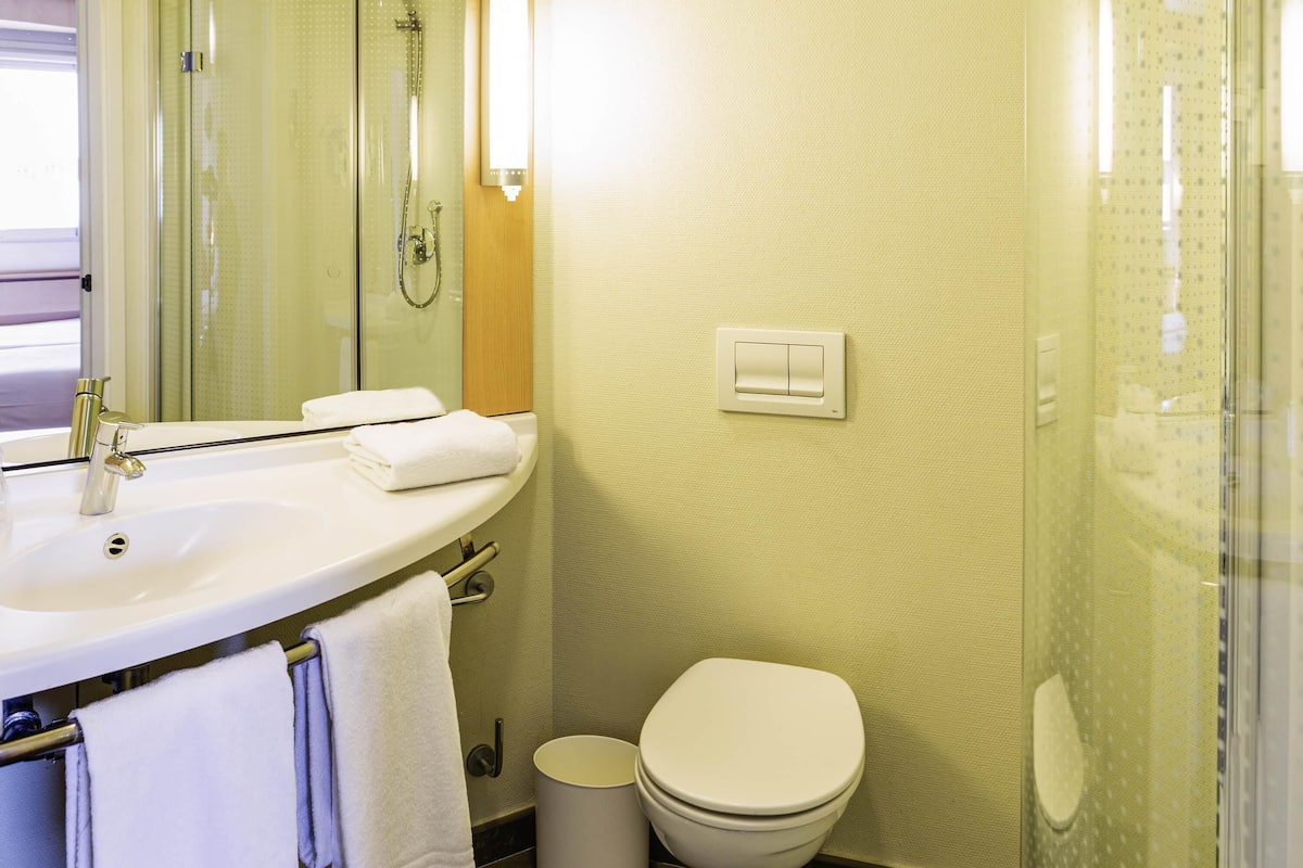 Une salle de bain avec un lavabo blanc, un miroir, un porte-serviettes, des toilettes et un espace douche.