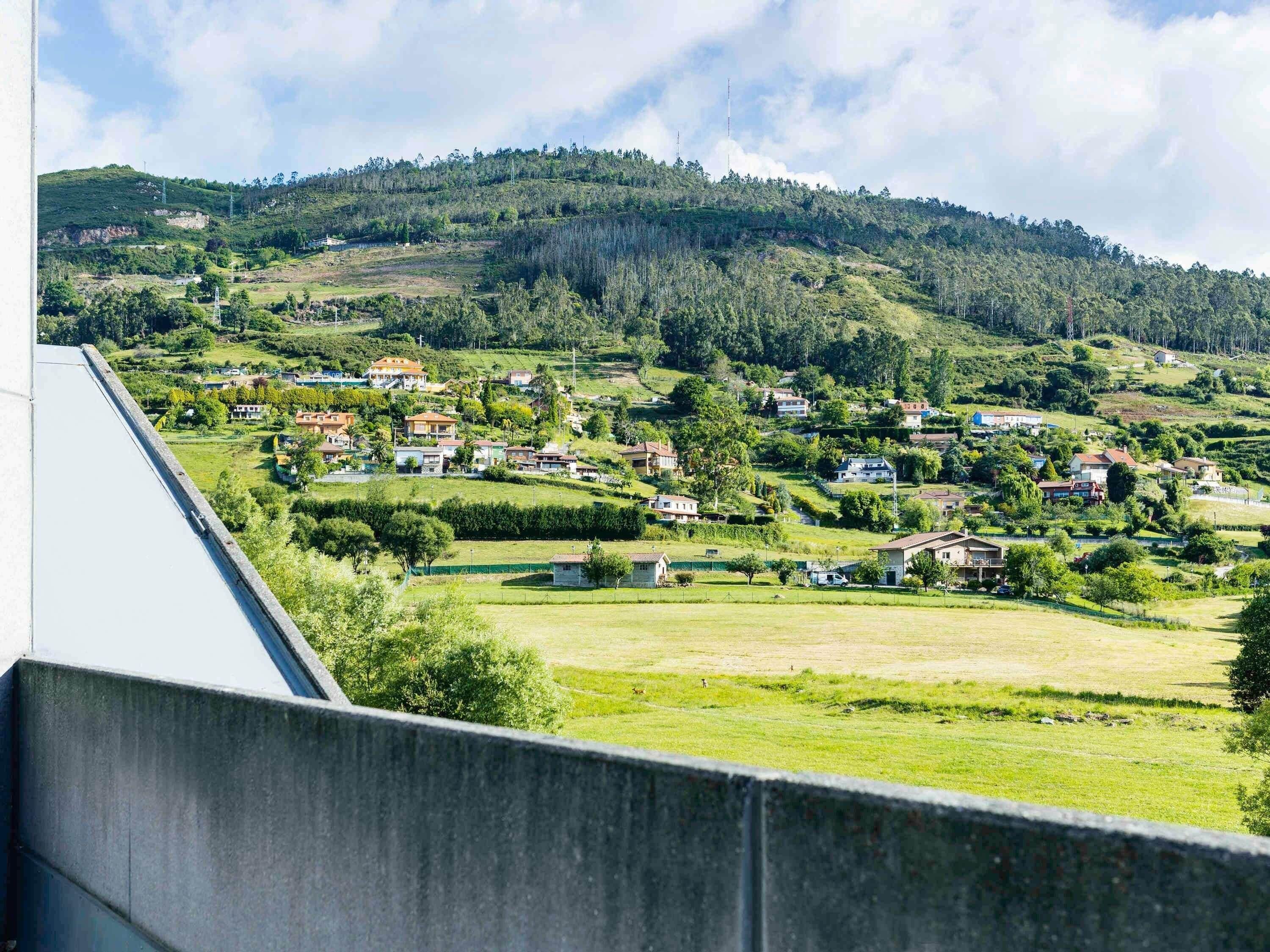 Una zona residencial con casas, campos verdes y una colina al fondo.