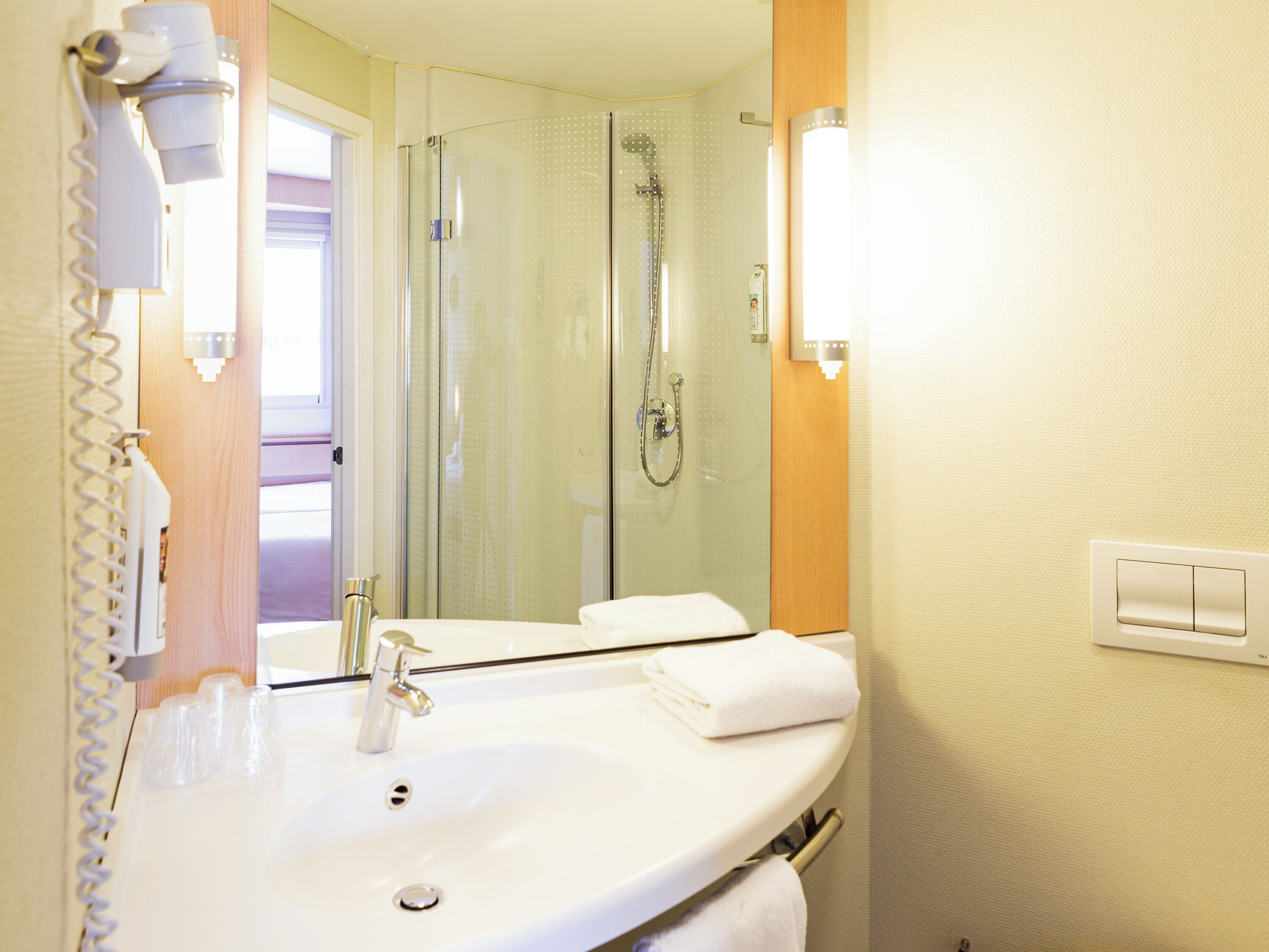 A bathroom with a sink, mirror, towel rack, and shower.