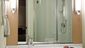 Ein Badezimmer mit Duschkabine aus Glas, einem weißen Waschbecken mit chromfarbenem Wasserhahn und einem Spiegel über dem Waschbecken.
