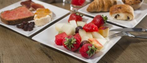 Une table dressée pour le petit-déjeuner, avec des assiettes de toasts, des fruits, des croissants et un verre de jus d’orange.