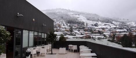 A rooftop terrace with white tables and chairs, overlooking a snow-covered landscape.