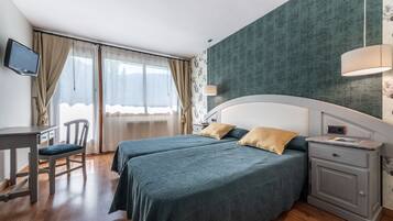 Habitación de hotel con dos camas, un escritorio, una silla, un televisor y una mesita de noche con una lámpara.