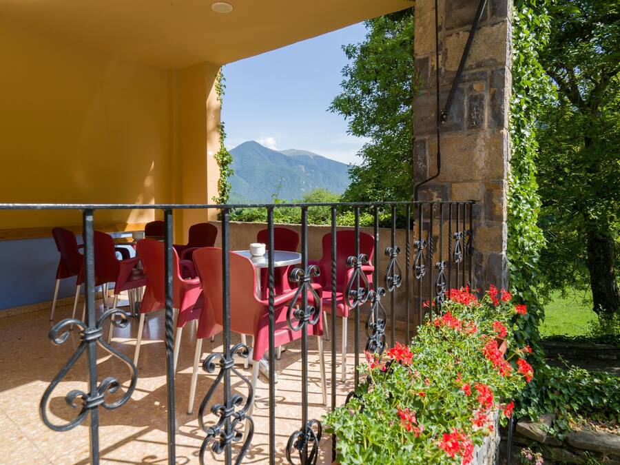 Una terraza con sillas y mesas rojas, un muro de piedra y vistas a montañas.
