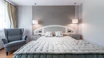 Un dormitorio moderno con una cama capitonada, dos lámparas de noche, un sillón gris y papel tapiz estampado.