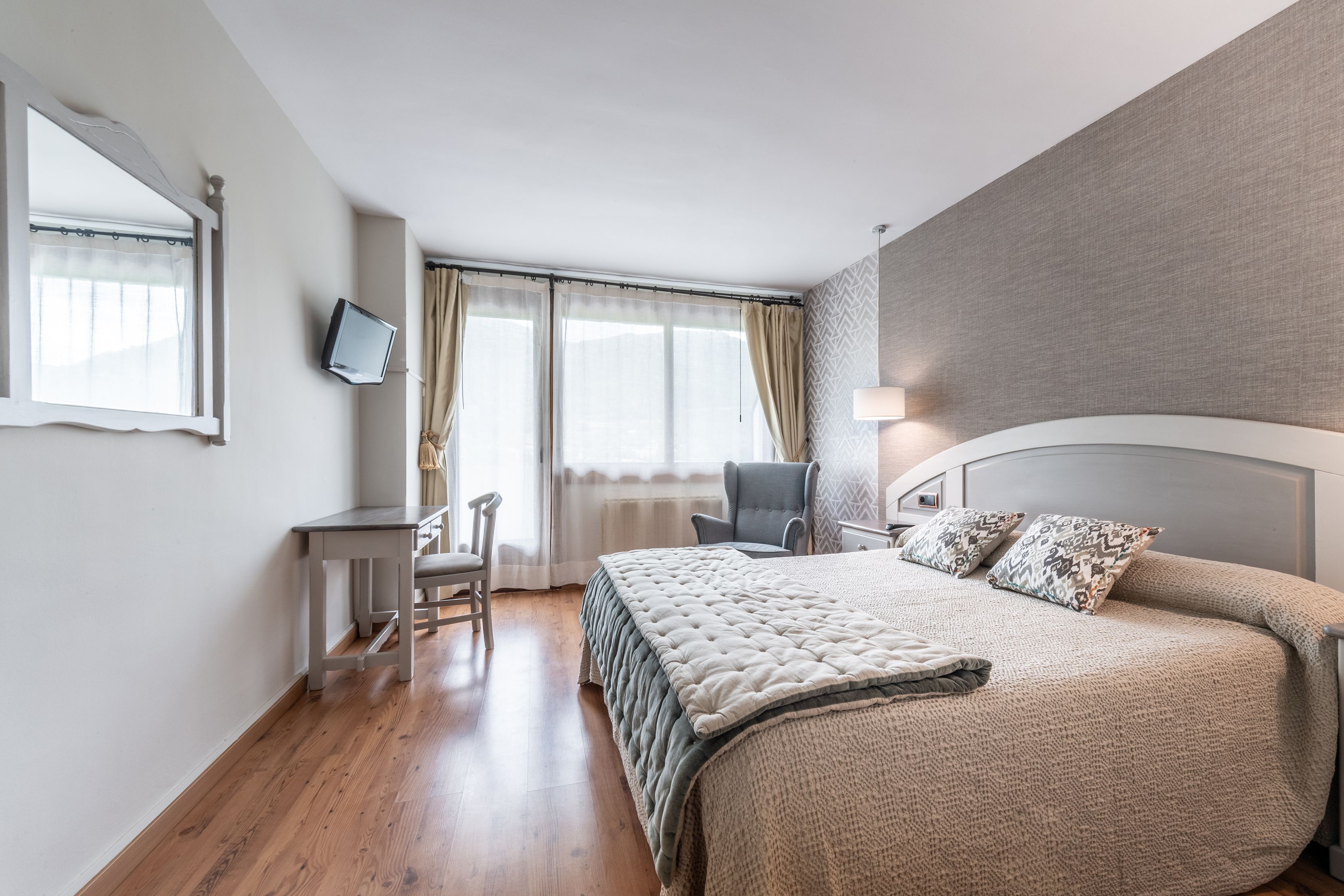 Un dormitorio con una cama grande, un escritorio, una silla, un televisor y una ventana con cortinas.