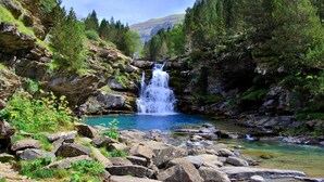 Paisaje natural con una cascada, terreno rocoso y una piscina azul cristalina.